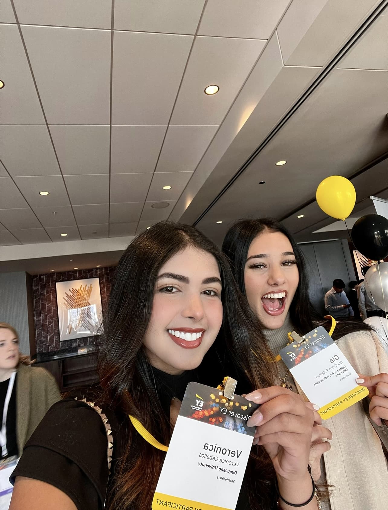 Two students smiling at an EY event holding conference badges.