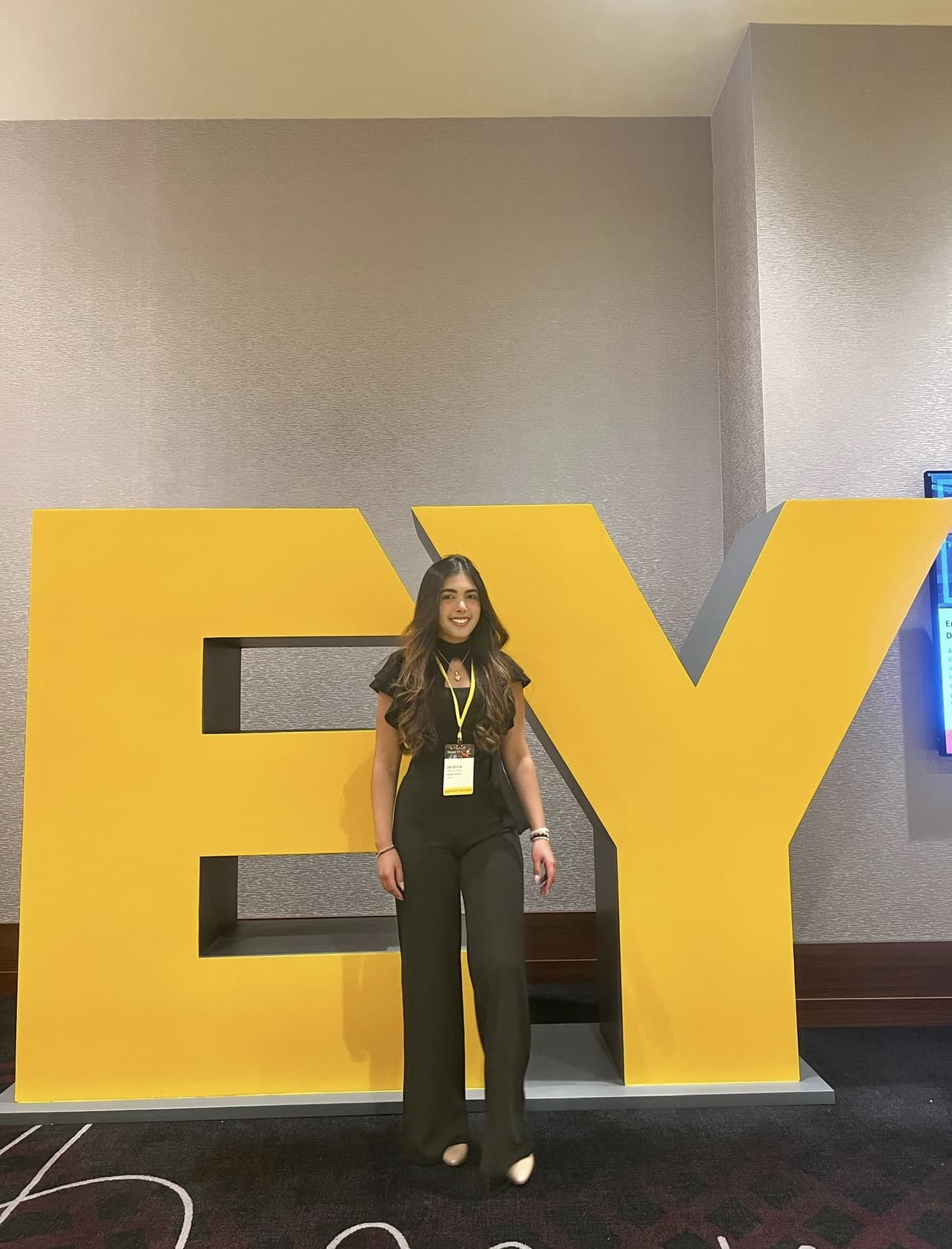 A student standing in front of large yellow EY letters at an event.